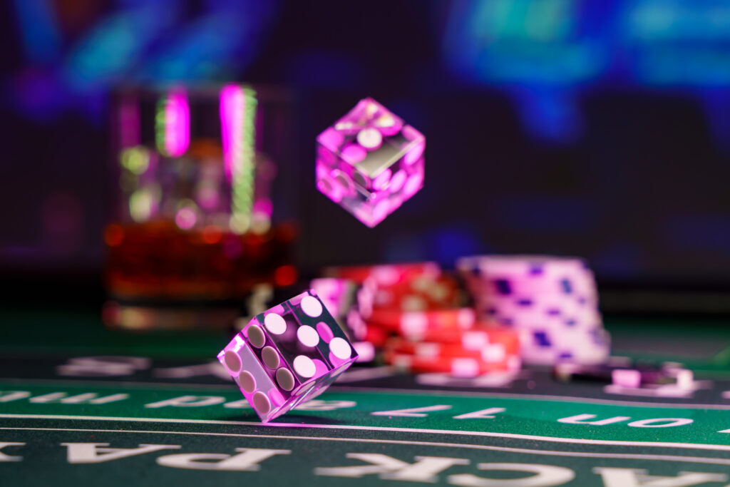 Close up of craps dice on mid-roll. In the background are casino chips and a glass, both of which are blurred.