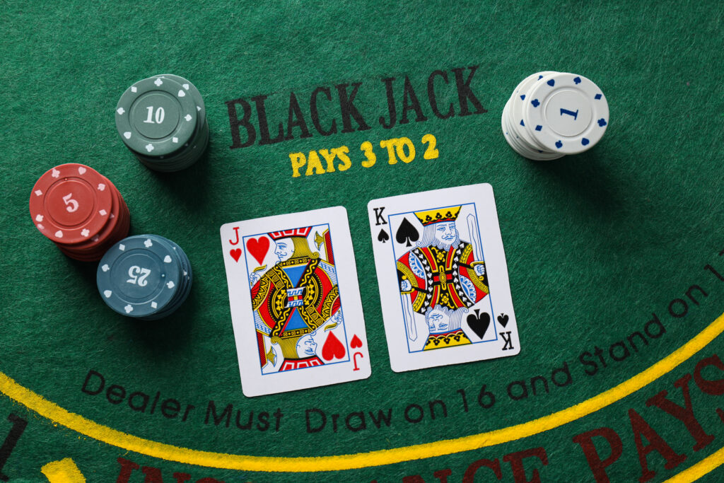Blackjack table with a pile of green, red and blue casino chips on the left, and a pile of white casino chips on the right. In the centre is a Jack of Hearts and a King of Spades.