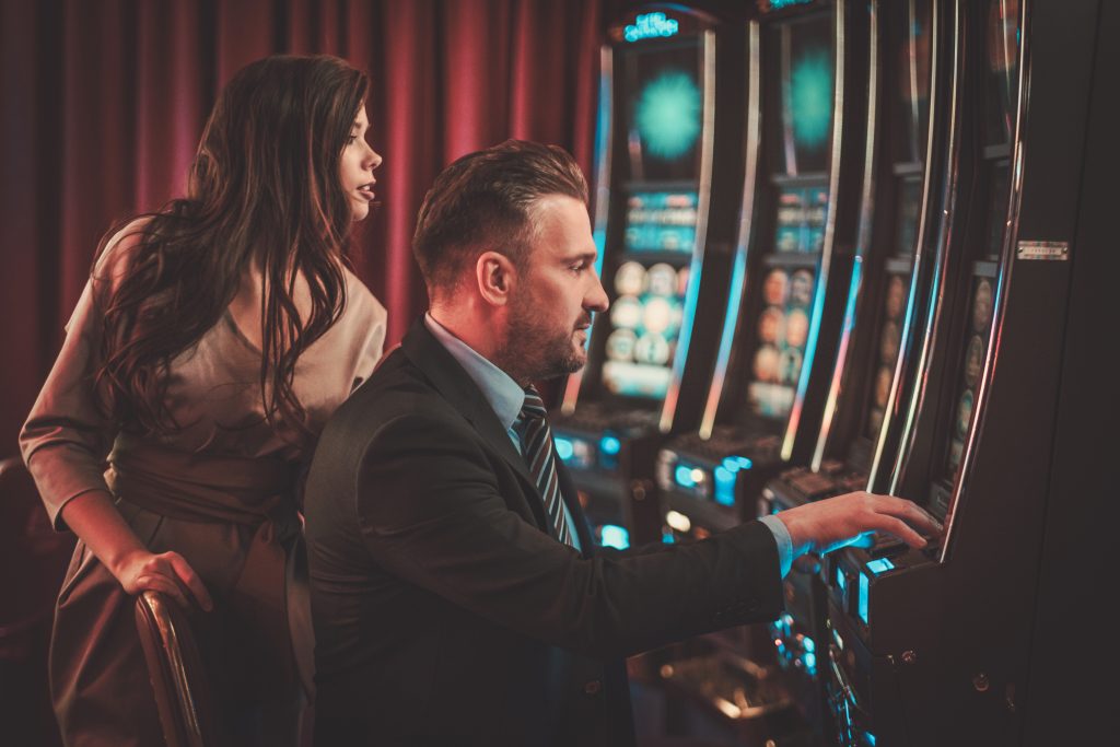 A photo of two people playing on a slot machine in a casino.