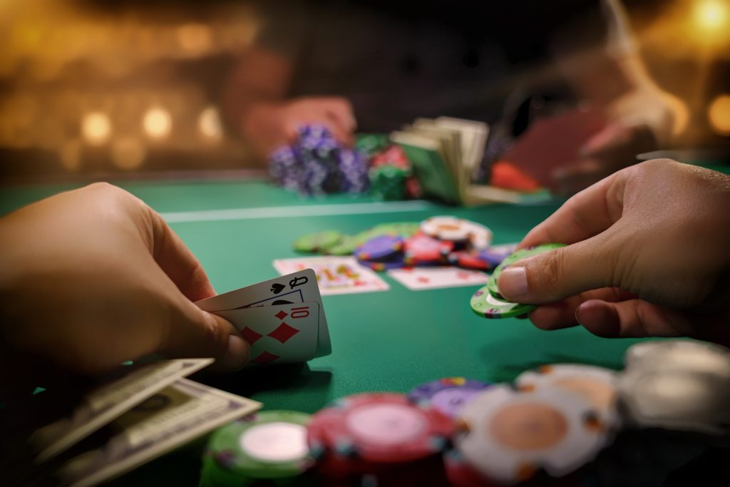 A photo of two people playing poker with casino chips and cards in the middle of the table.