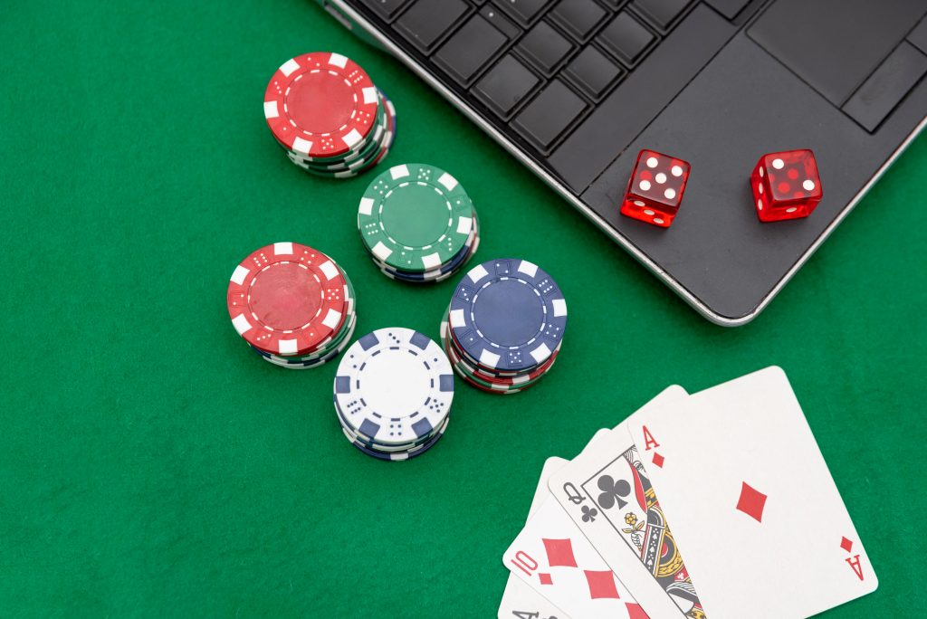 A photo of a laptop next to casino chips, dice and playing cards.