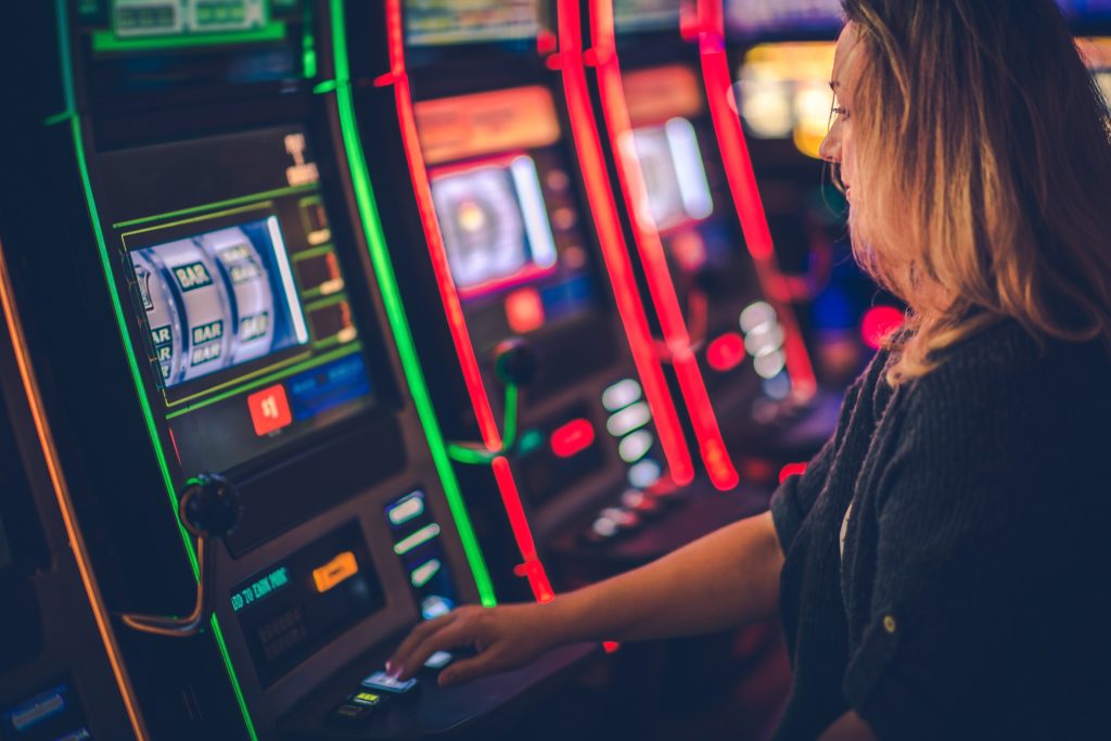 A woman playing a slot machine in a casino with bar symbols displayed on the screen.