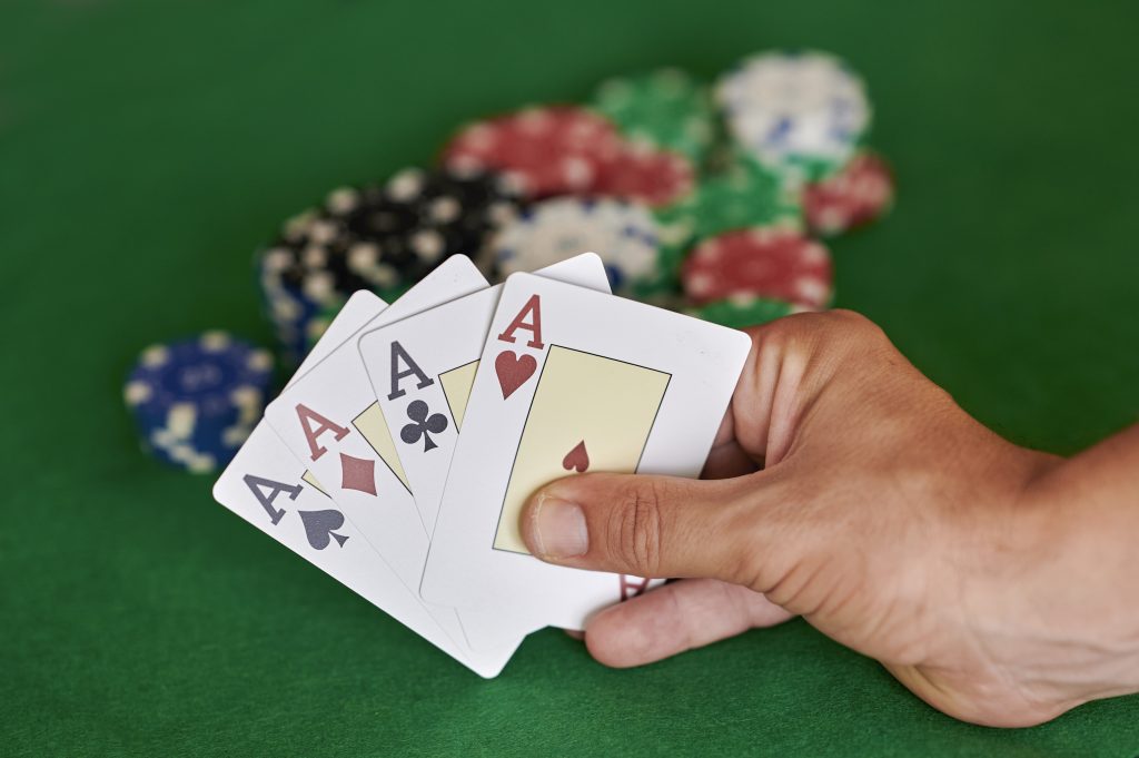 A photo of a person holding four aces next to a pile of casino chips.