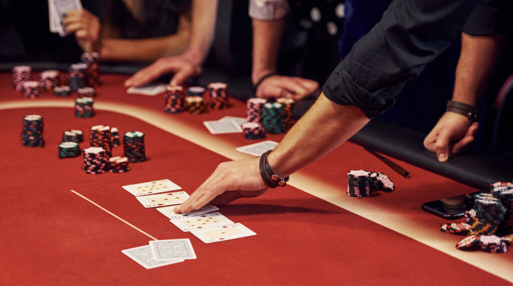 Close up of casino players hands and red casino table with casino chips and playing cards on it.