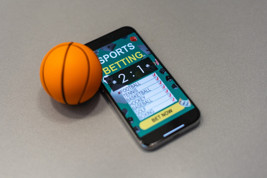 A smartphone with application for sport bets and a small basketball ball beside it.