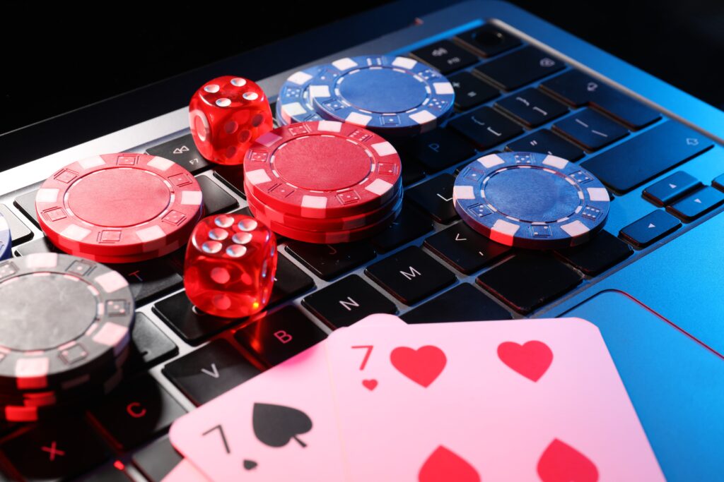 Close up of playing cards, casino chips, dice on a laptop.