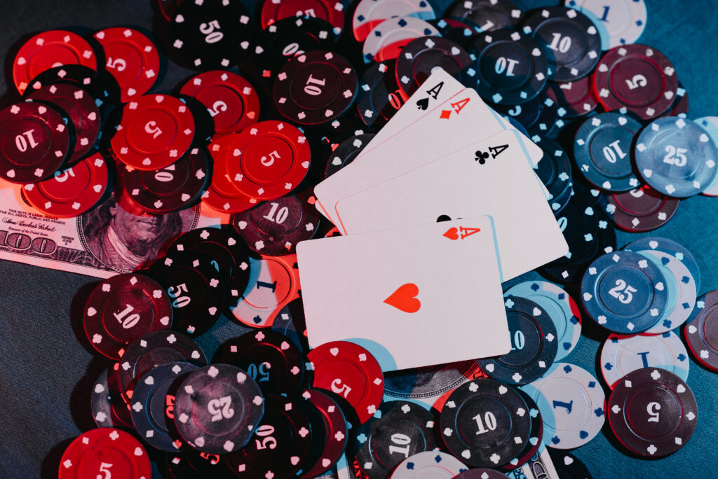 Four Aces on top of a pile of casino chips. Under some chips is a $100 bill.